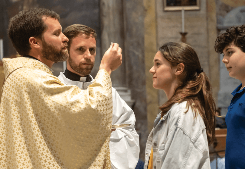 Catholic priest giving Holy Communion to youth